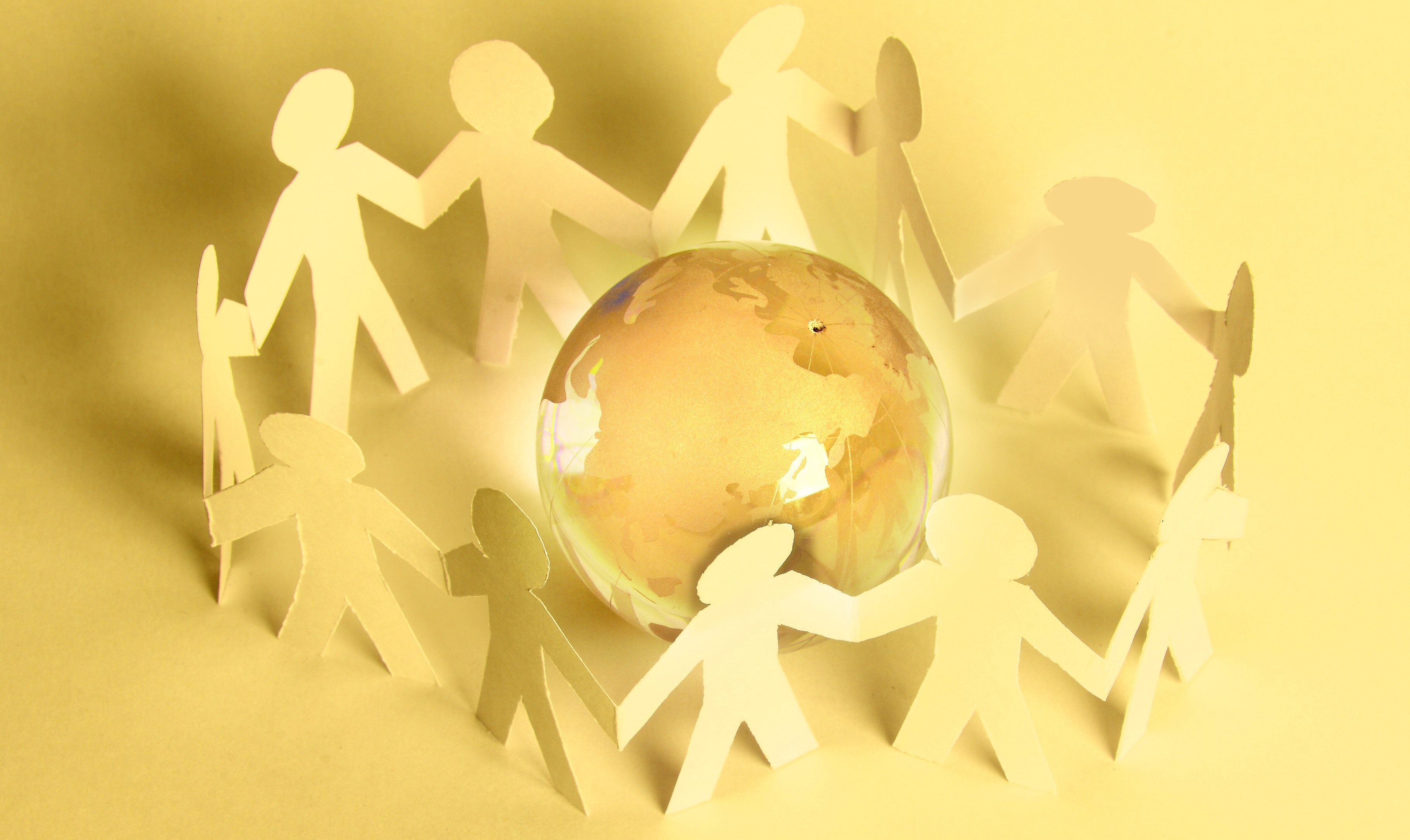 Paper people standing in a circle around glass globe